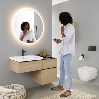 Bărbatul se priveşte într-o oglindă rotundă iluminată Geberit Option Bărbatul se priveşte într-o oglindă rotundă iluminată Geberit Option