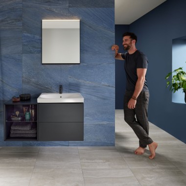 Bărbatul se sprijină de perete în baia albastră dotată cu lavoar Geberit Mix & Match Bărbatul se sprijină de perete în baia albastră dotată cu lavoar Geberit Mix & Match