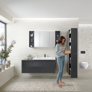 Femeia deschide un dulap înalt cu mult spațiu de depozitare în baie cu mobilier de baie Geberit Acanto Femeia deschide un dulap înalt cu mult spațiu de depozitare în baie cu mobilier de baie Geberit Acanto