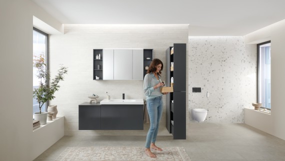 Femeia deschide un dulap înalt cu mult spațiu de depozitare în baie cu mobilier de baie Geberit Acanto Femeia deschide un dulap înalt cu mult spațiu de depozitare în baie cu mobilier de baie Geberit Acanto