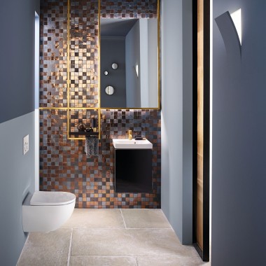 Vedere într-o baie modernă pentru oaspeți, cu un WC Acanto și o lavoar Acanto în fața unui panou de mozaic din spate