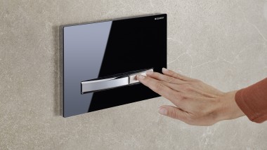 O mână activează spălarea pe o clapetă de acționare Sigma50 neagră (© Geberit)