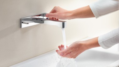 O femeie deschide robinetul şi simte presiunea şi temperatura apei