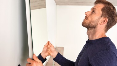 Bărbat care agață o oglindă Geberit Option în timpul renovării unei băi