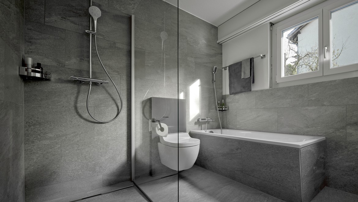 Un vas wc cu funcție de bideu între un duș la nivel cu podeaua și o cadă de baie