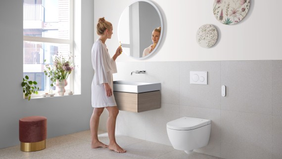 Femeie într-o baie albă cu obiecte sanitare din ceramică și mobilier de baie (© Geberit)