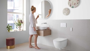 Femeie într-o baie albă cu obiecte sanitare din ceramică și mobilier de baie (© Geberit)